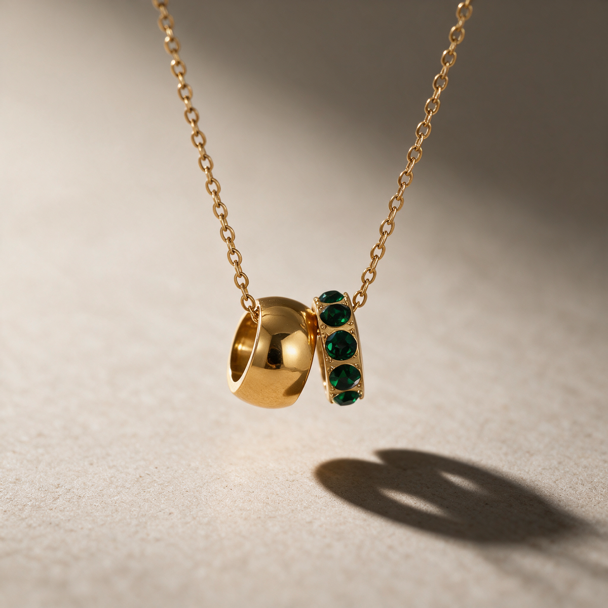 The Linked Birthstone Necklace in dark green — two interlocking rings pendant, one solid and one crystal, on a fine chain.
